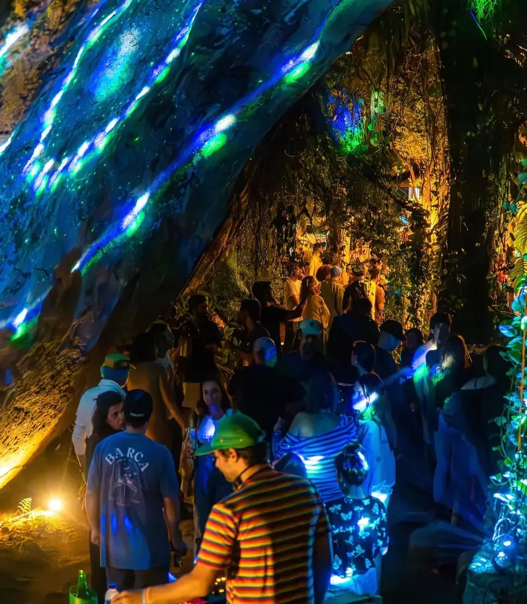Festa com luzes coloridas sob as pedras e a mata na Casa Barca