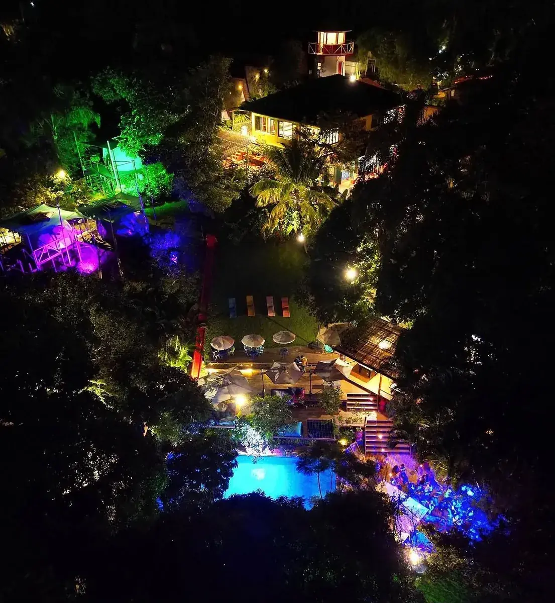 Vista aérea noturna do Hostel da Vila iluminado no meio da mata