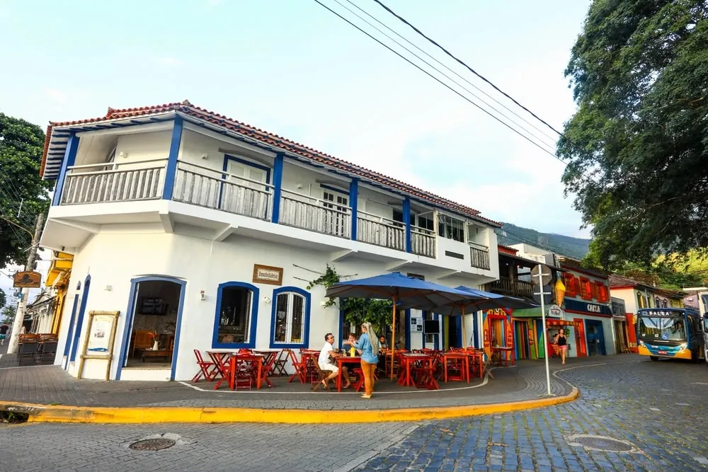 Casarão colonial branco e azul com mesas na calçada, na Vila
