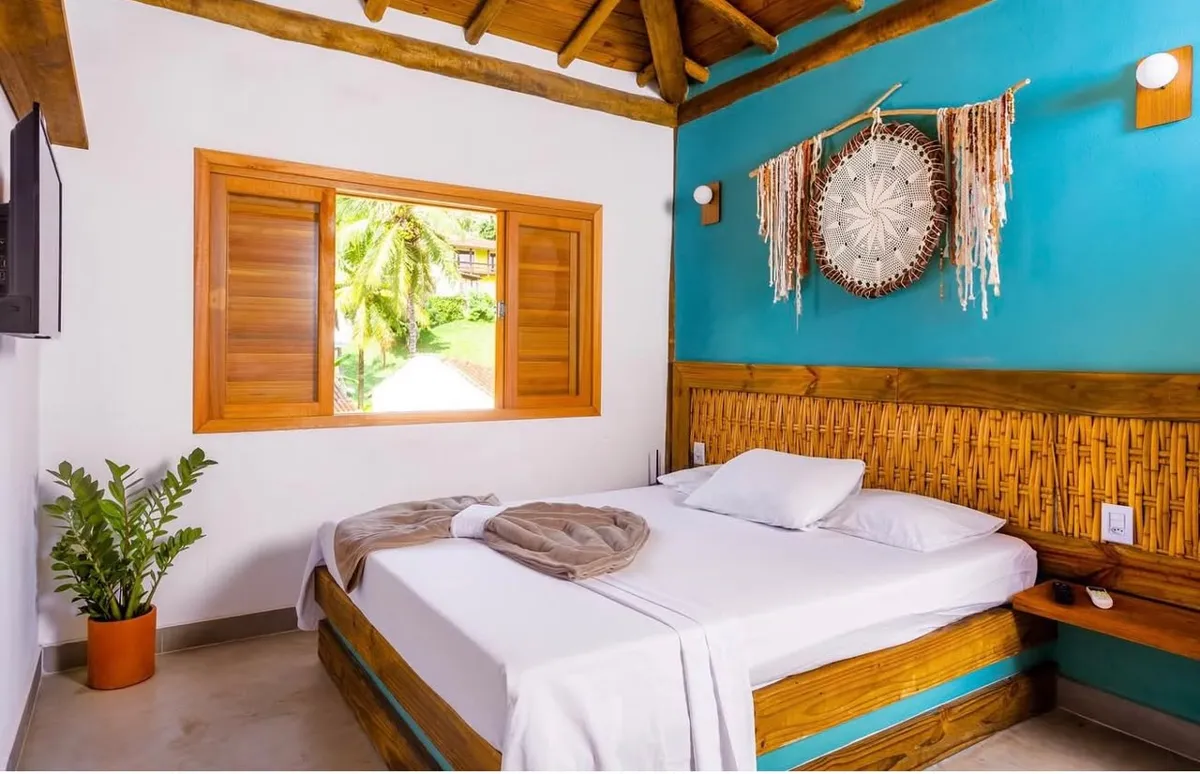 Suíte de casal com decoração artesanal e janela para o jardim, na Casa Maembippe