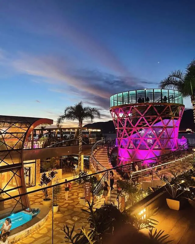 Área aberta do Mares Ilha Mall ao entardecer, com o mirante iluminado e o mar ao fundo
