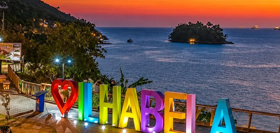 Letreiro Amo Ilhabela iluminado ao pôr do sol no Mirante do Piúva, com a Ilha das Cabras ao fundo