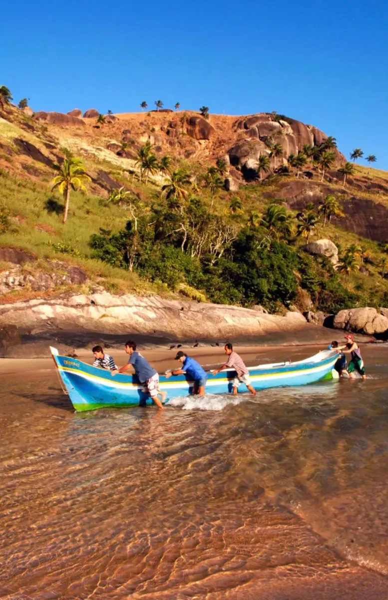 Pescadores empurrando uma canoa caiçara colorida na Praia do Bonete
