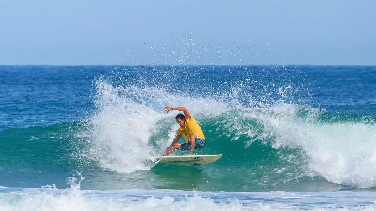 Surfista de lycra amarela fazendo uma batida na onda